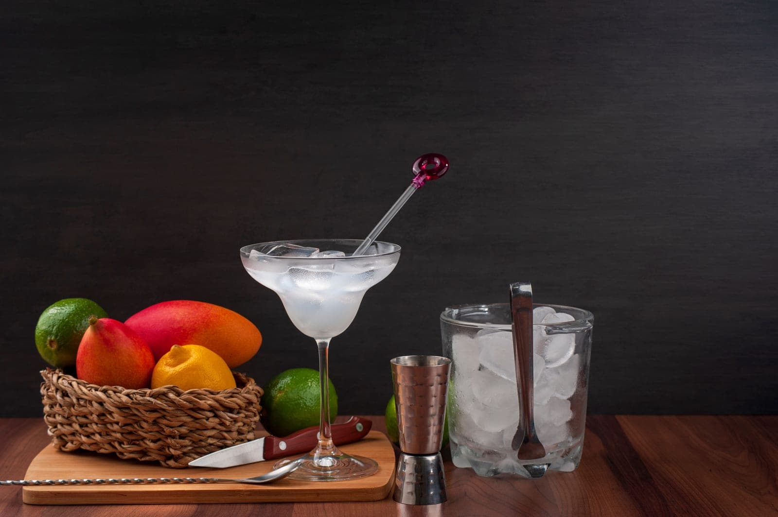 A jigger, ice bucket and finished cocktail set out on a wooden board