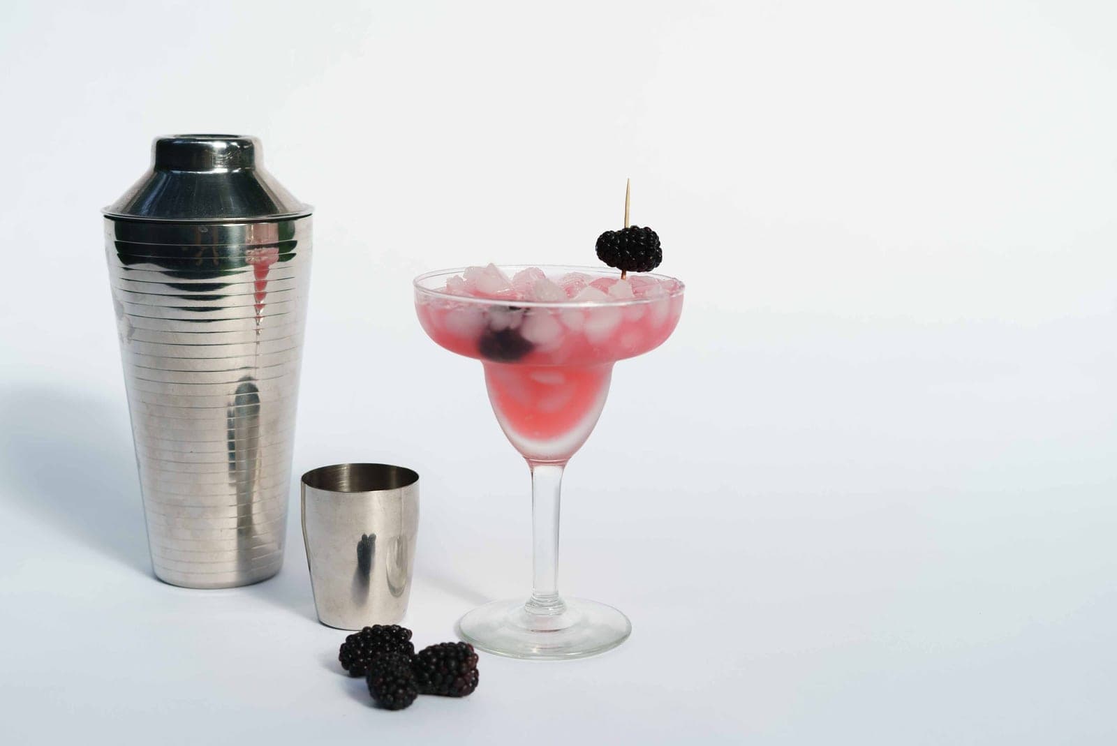 A cocktail shaker and a finished drink in a coupe on a white background